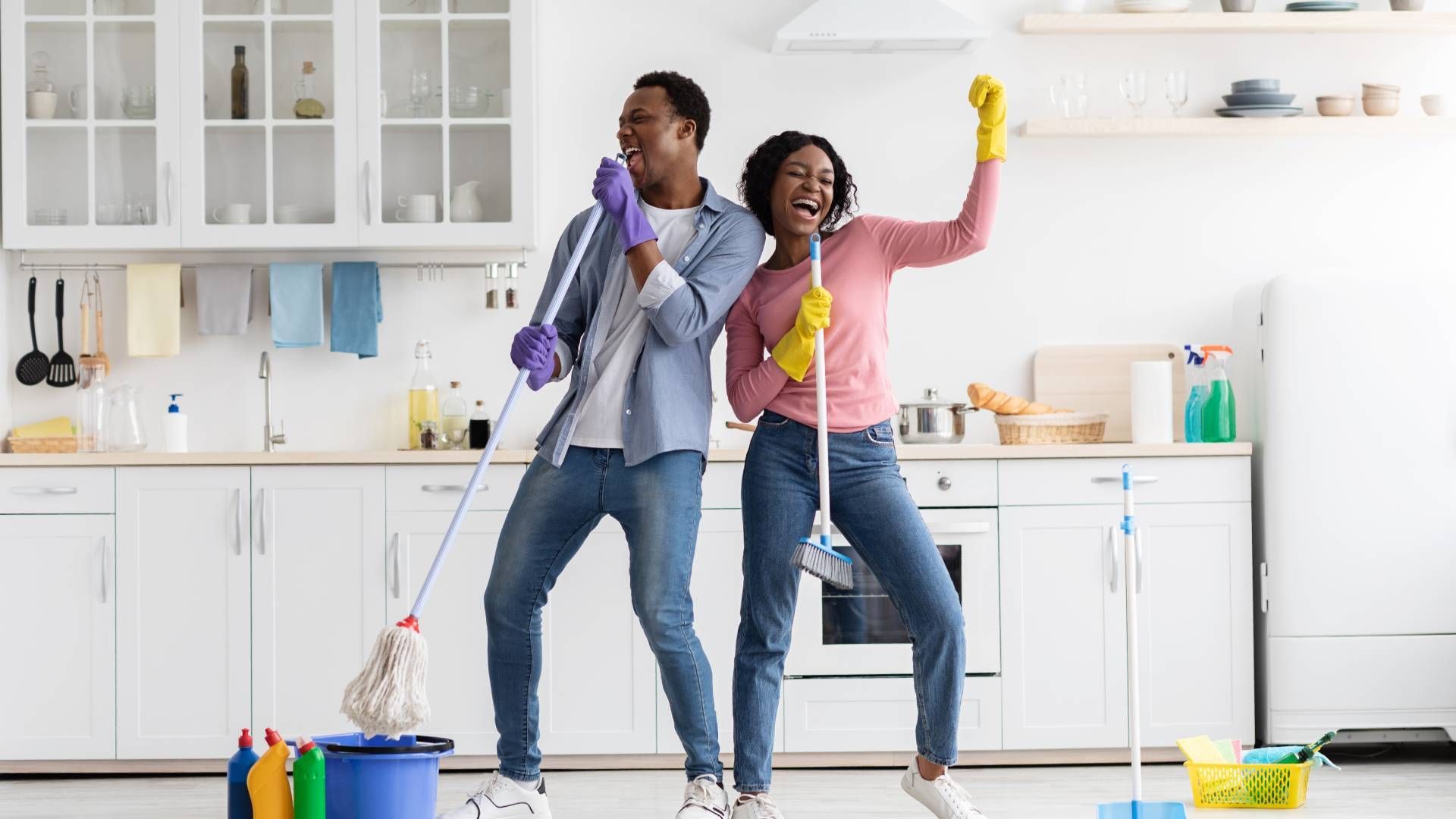 A man and a woman are dancing in a kitchen while cleaning the floor.