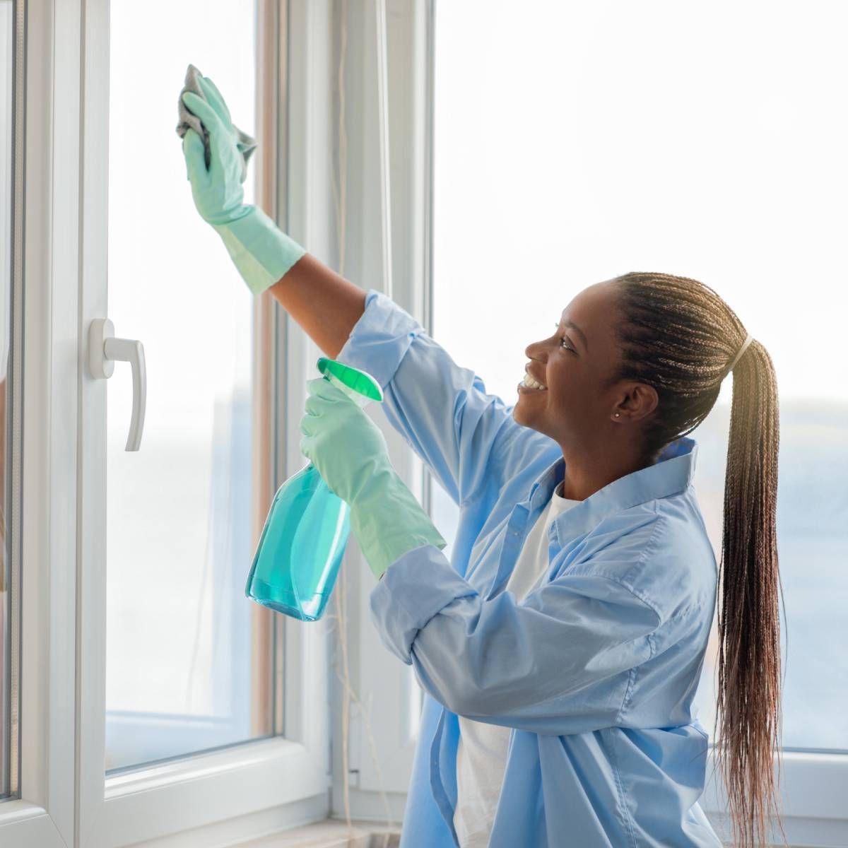 A woman is cleaning a window with a spray bottle and a cloth.