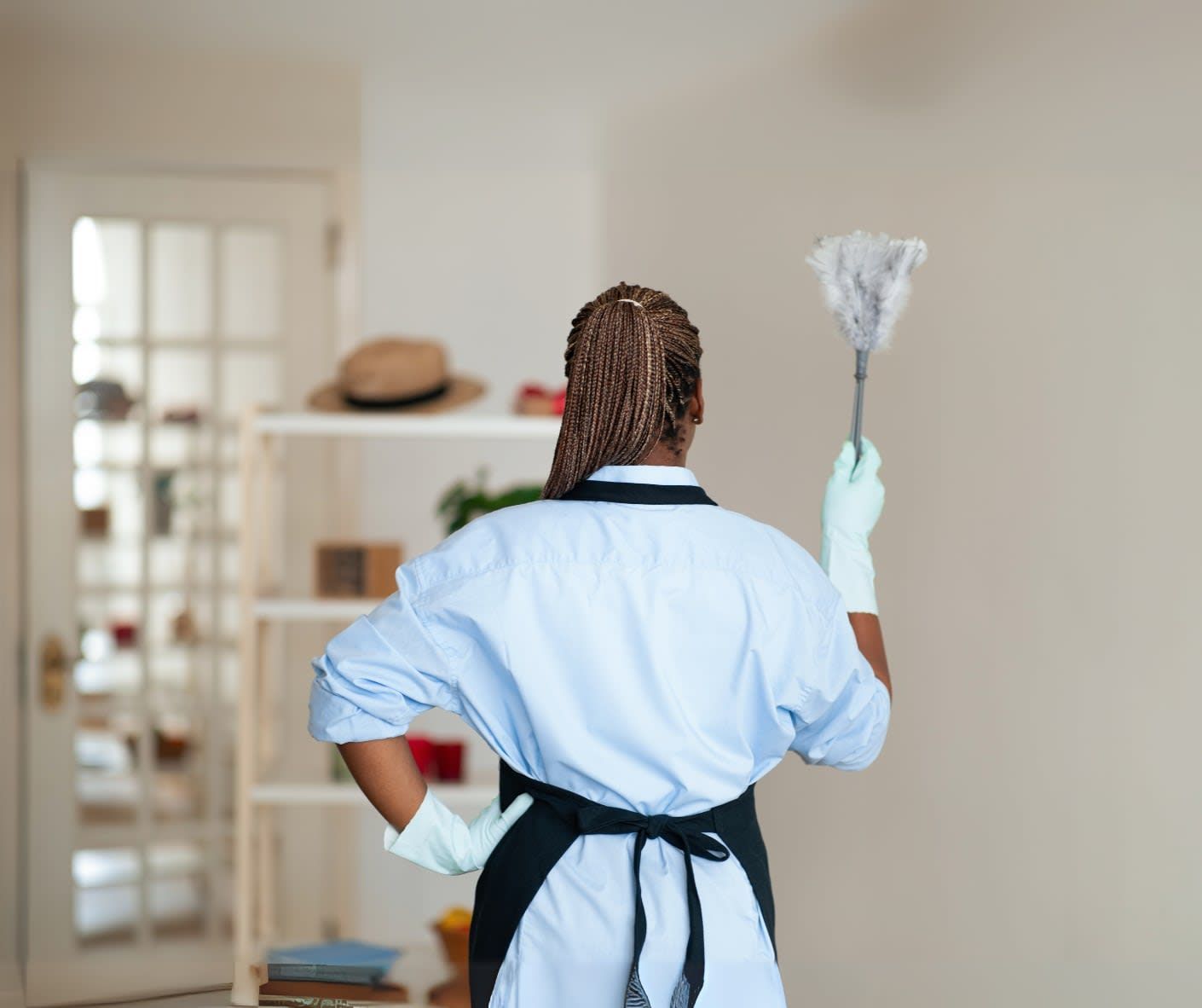 A woman is standing in a living room holding a duster.