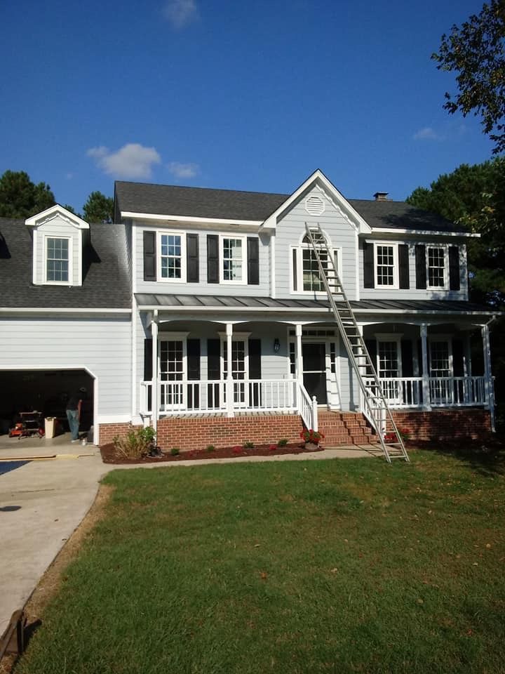 A large white house with black shutters and a ladder in front of it