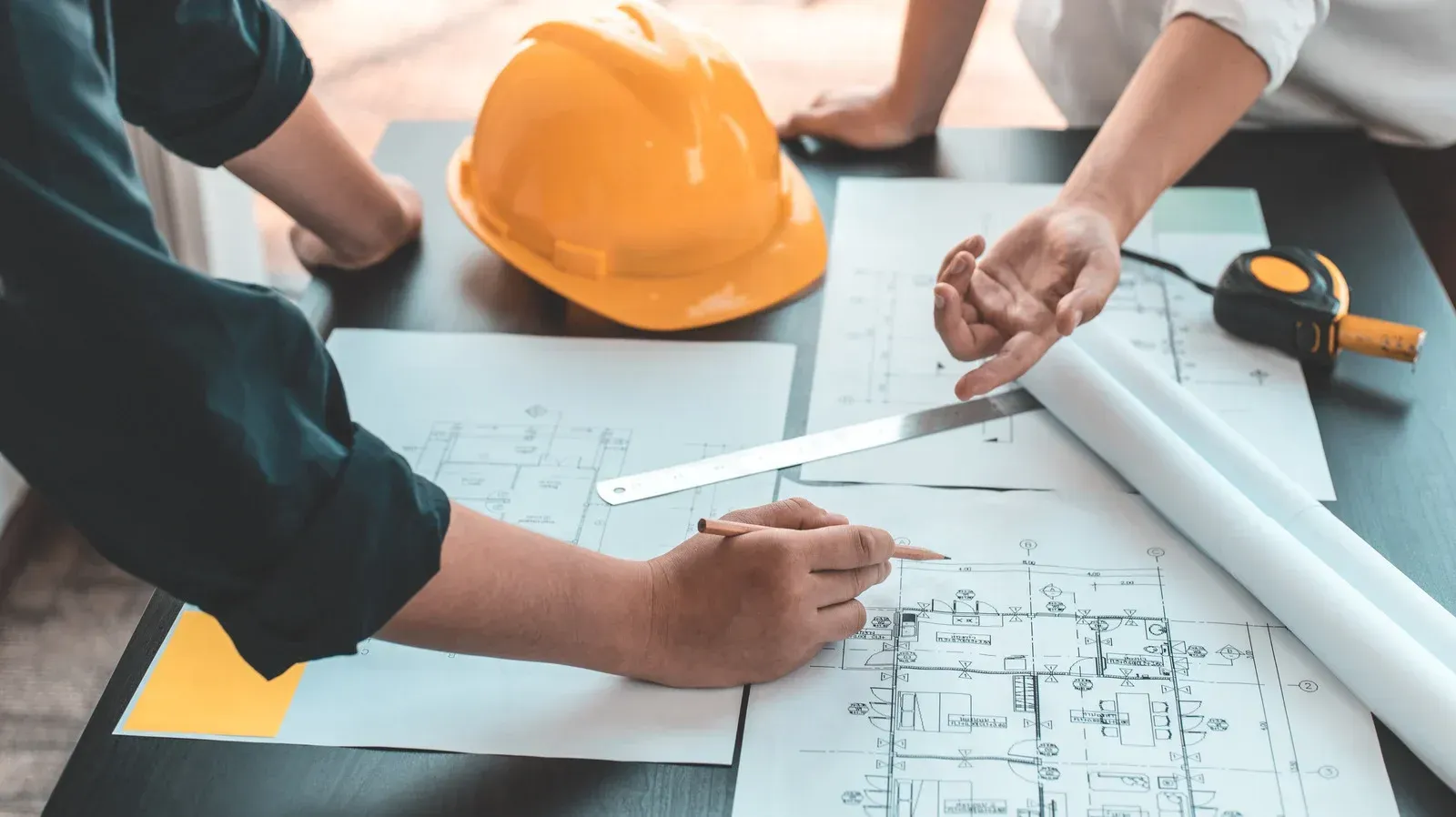 Two people reviewing blueprints, construction plans on a table, a yellow hard hat.