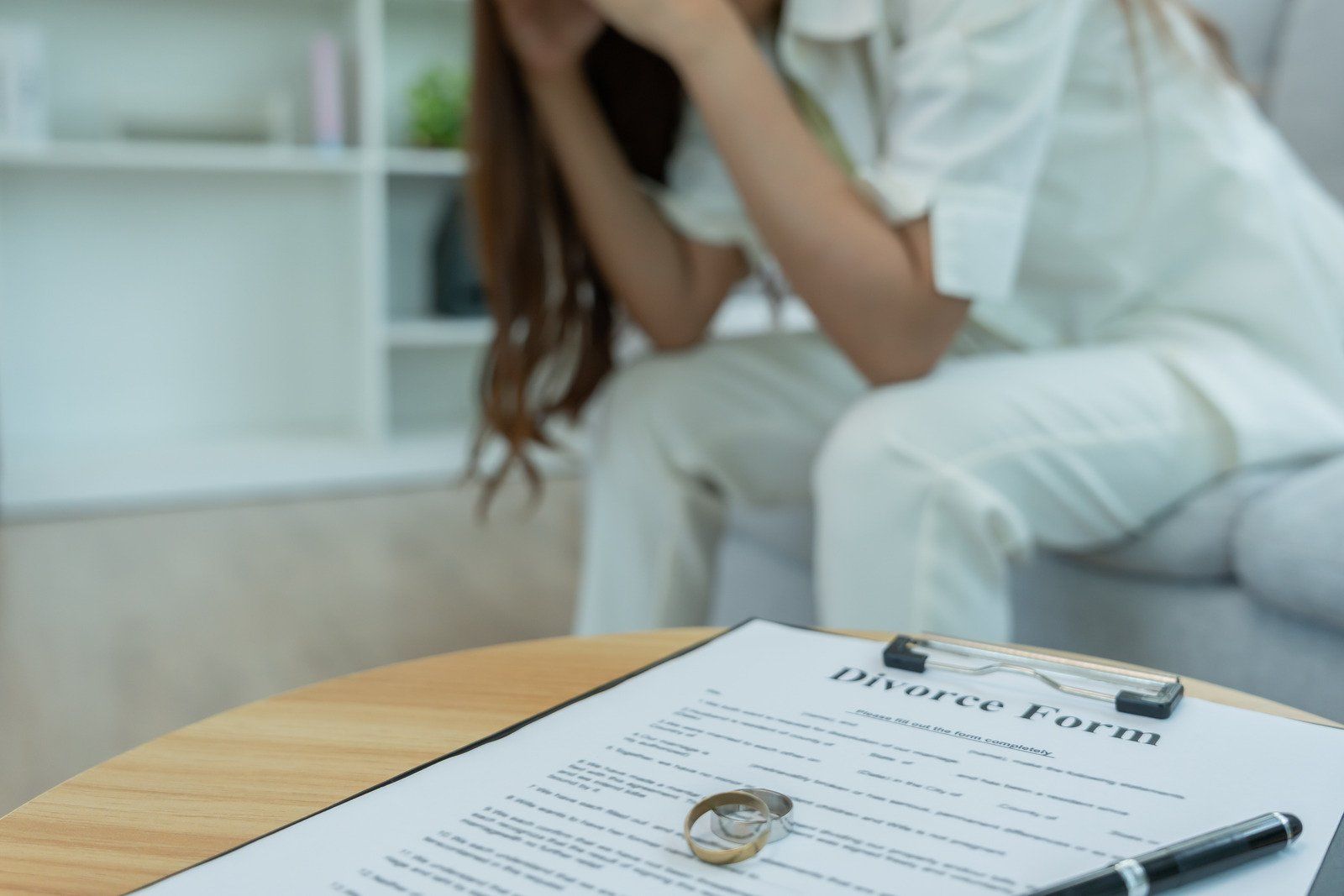 A person with head in hands, sitting near divorce form and wedding ring on a table.