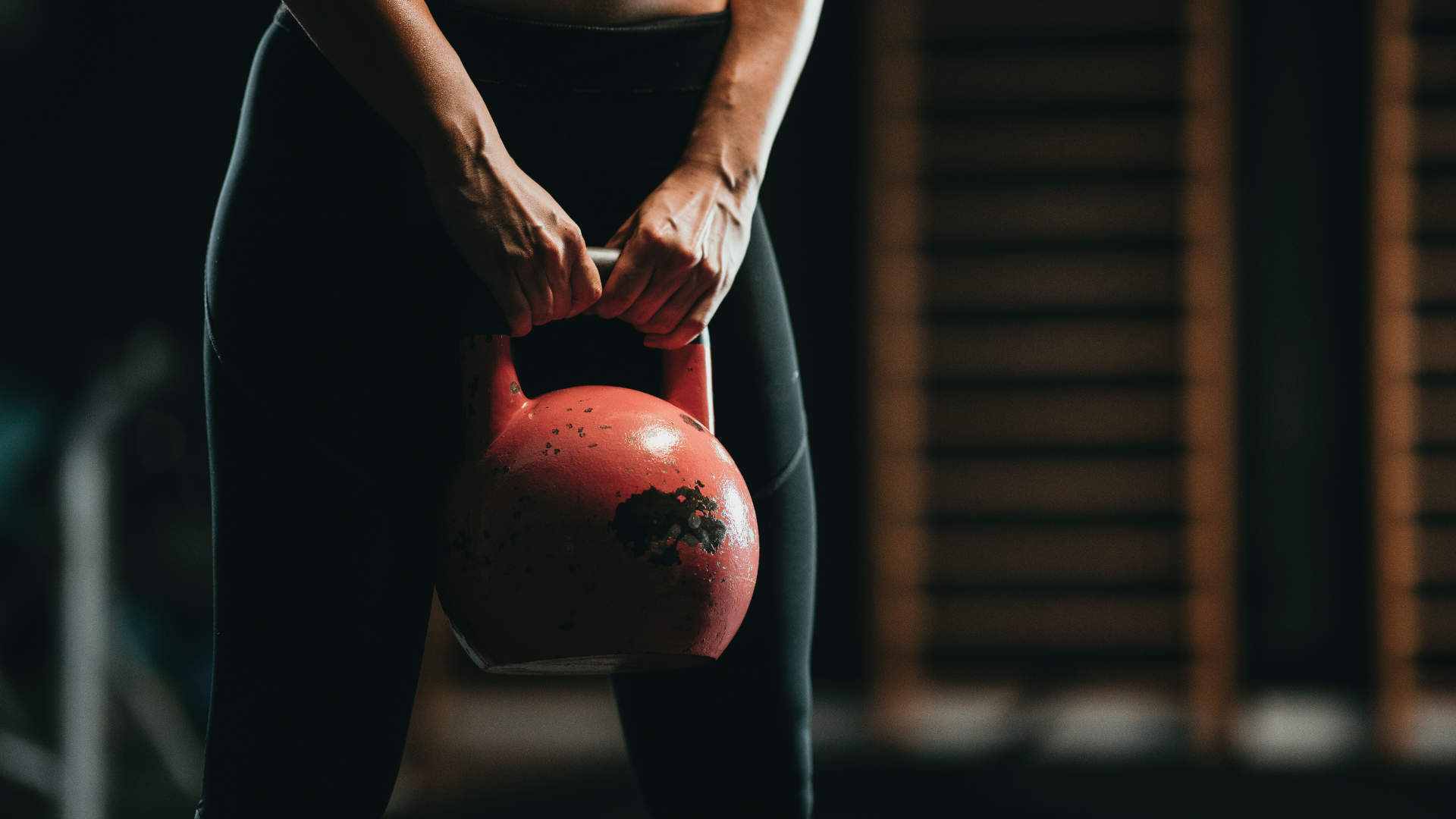 Woman holding a red kettlebell in a gym, wearing black workout gear.