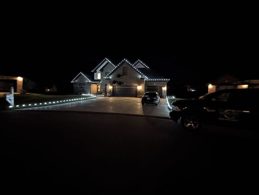 A house is lit up at night with cars parked in front of it.