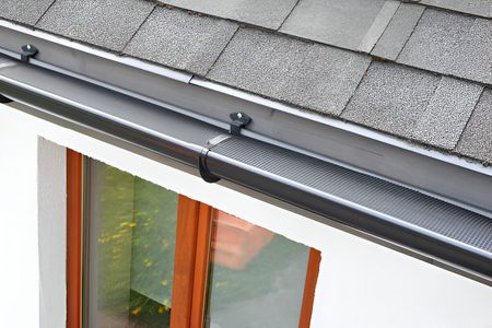 A close up of a gutter on a roof next to a window.