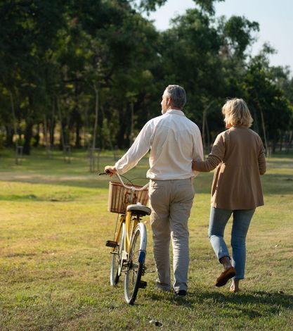 A man and a woman are walking in a park with a bicycle.