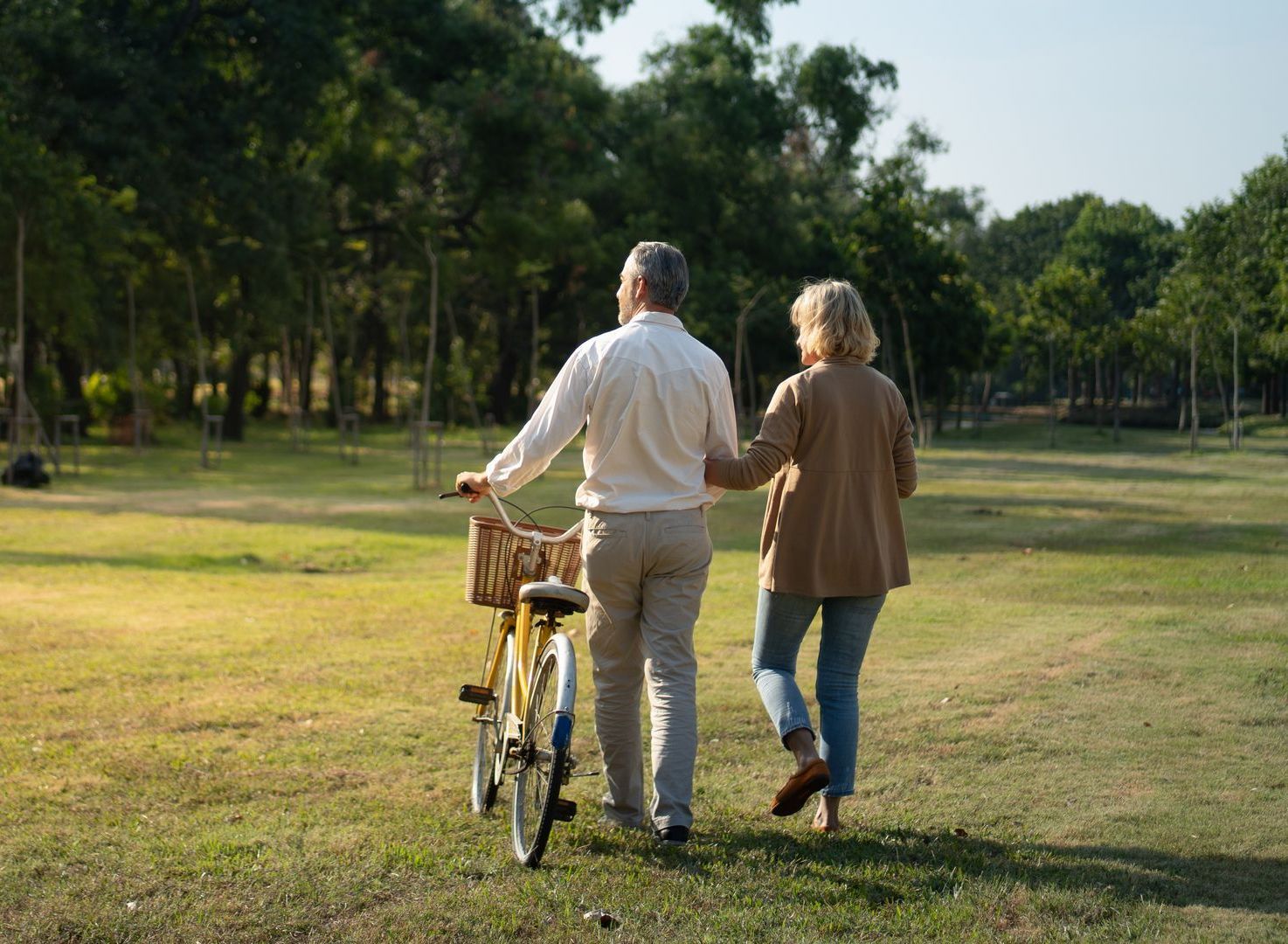 An elderly couple is walking with a bicycle in a park.