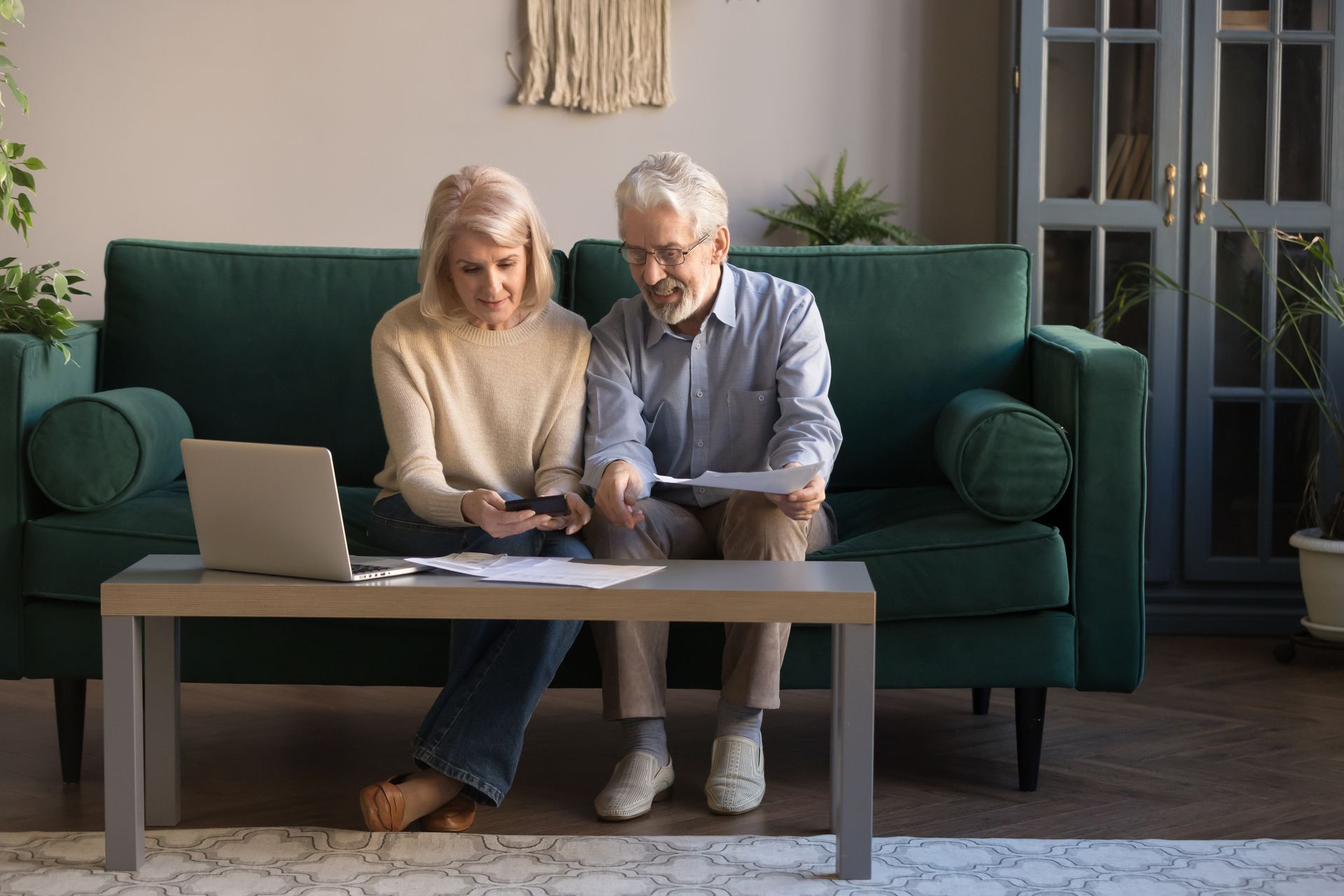 An elderly couple is sitting on a couch looking at a laptop.