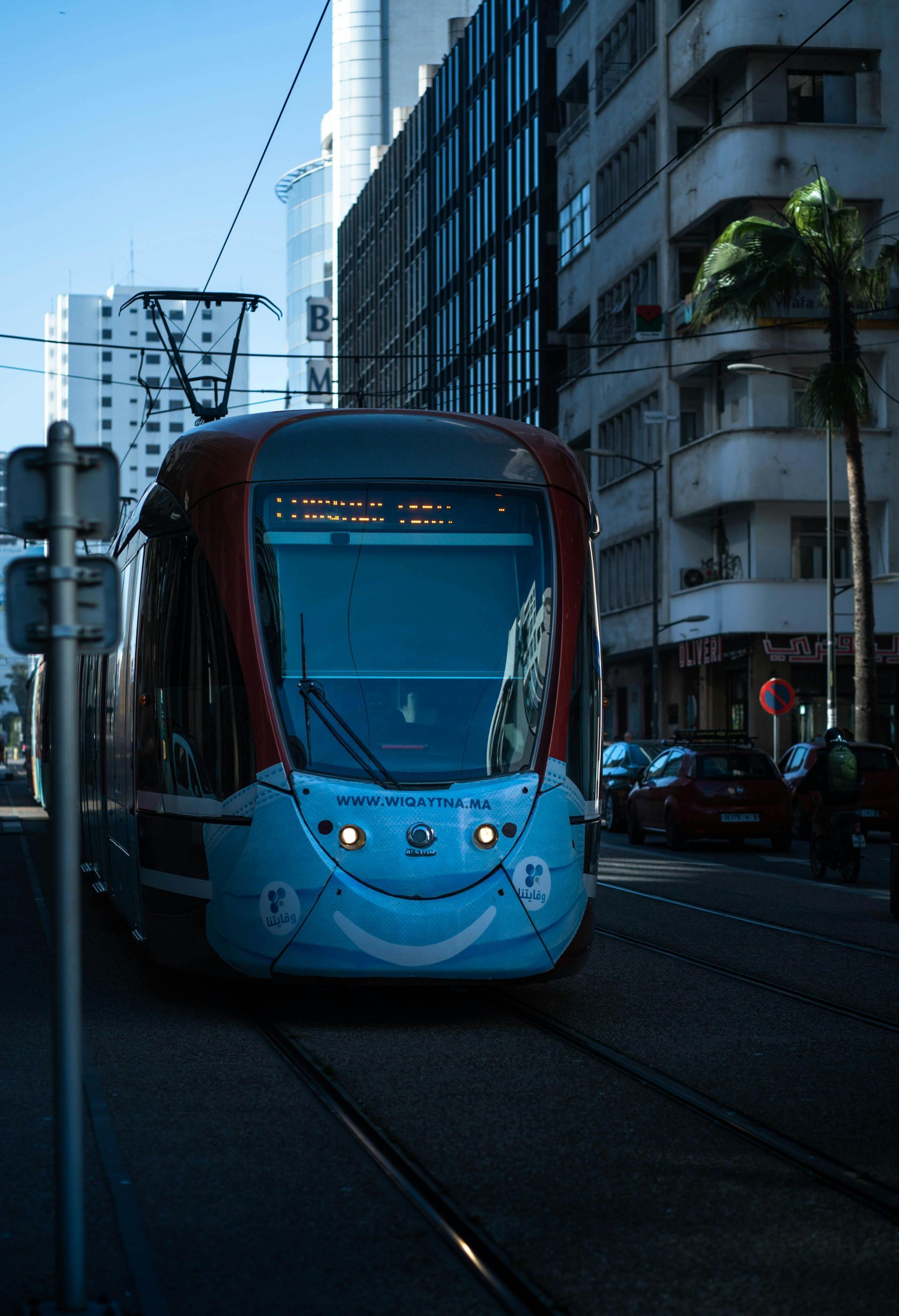 Um carrinho azul e vermelho com um rosto sorridente na frente está circulando por uma rua da cidade.