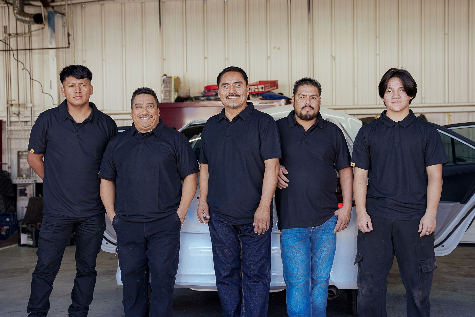 Five people in black shirts standing in front of a car inside a shop.