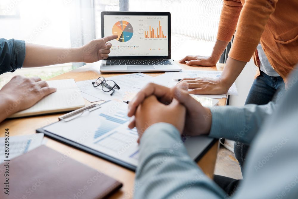 People collaborating around a laptop displaying charts and graphs, pointing and discussing data.
