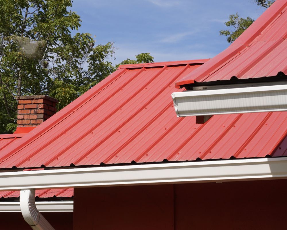 Red Metal Roof With White Gutters Against a Blue Sky, Brick Chimney, and Green Trees — Darren Smith Roofing In Glendale, NSW
