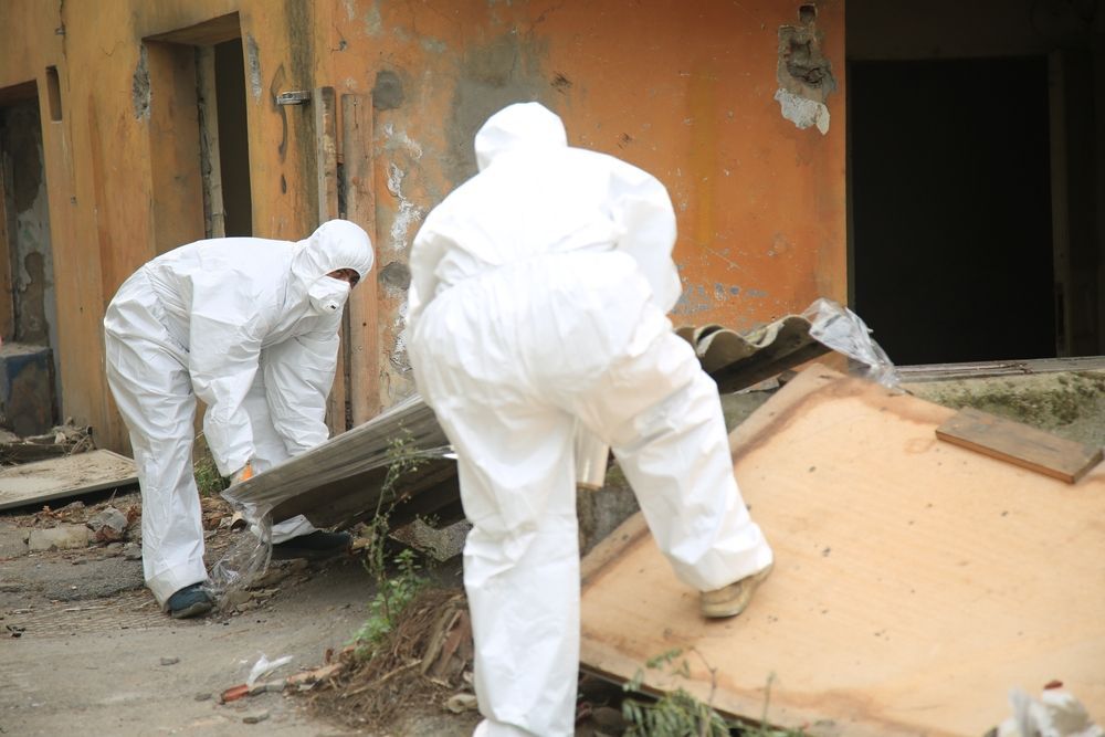 Two People in White Protective Suits Remove Debris From a Building — Darren Smith Roofing in Glendale, NSW