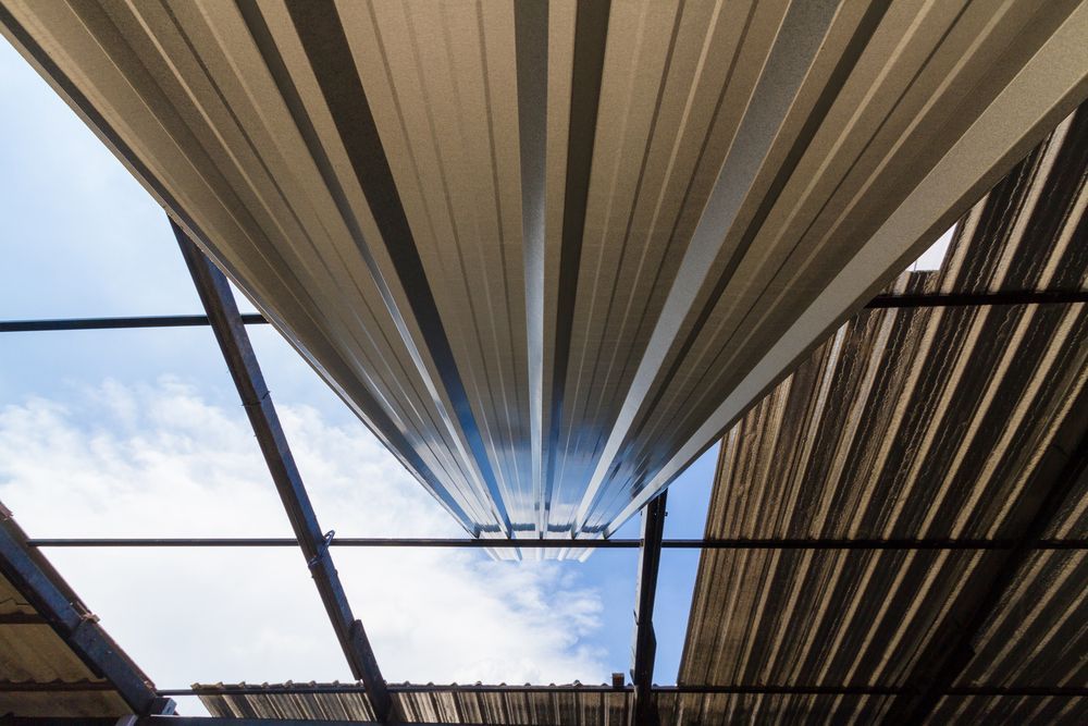 Looking Up at a Torn Metal Roof, Showing Blue Sky, Beams, and Contrasting Light — Darren Smith Roofing In Glendale, NSW