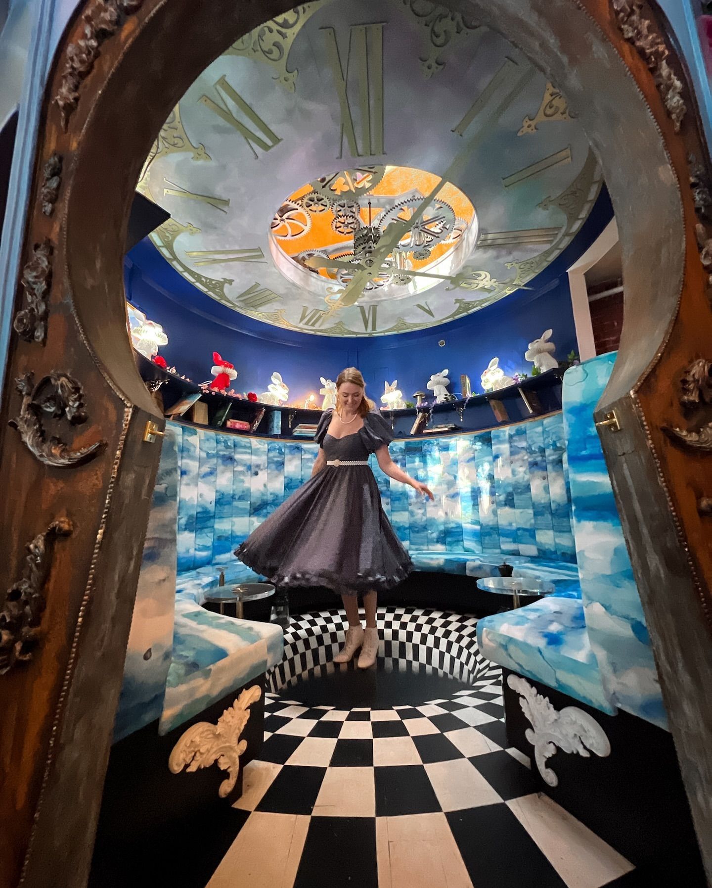 Woman in dress, mid-air, in a surreal room with checkered floor and clock ceiling.