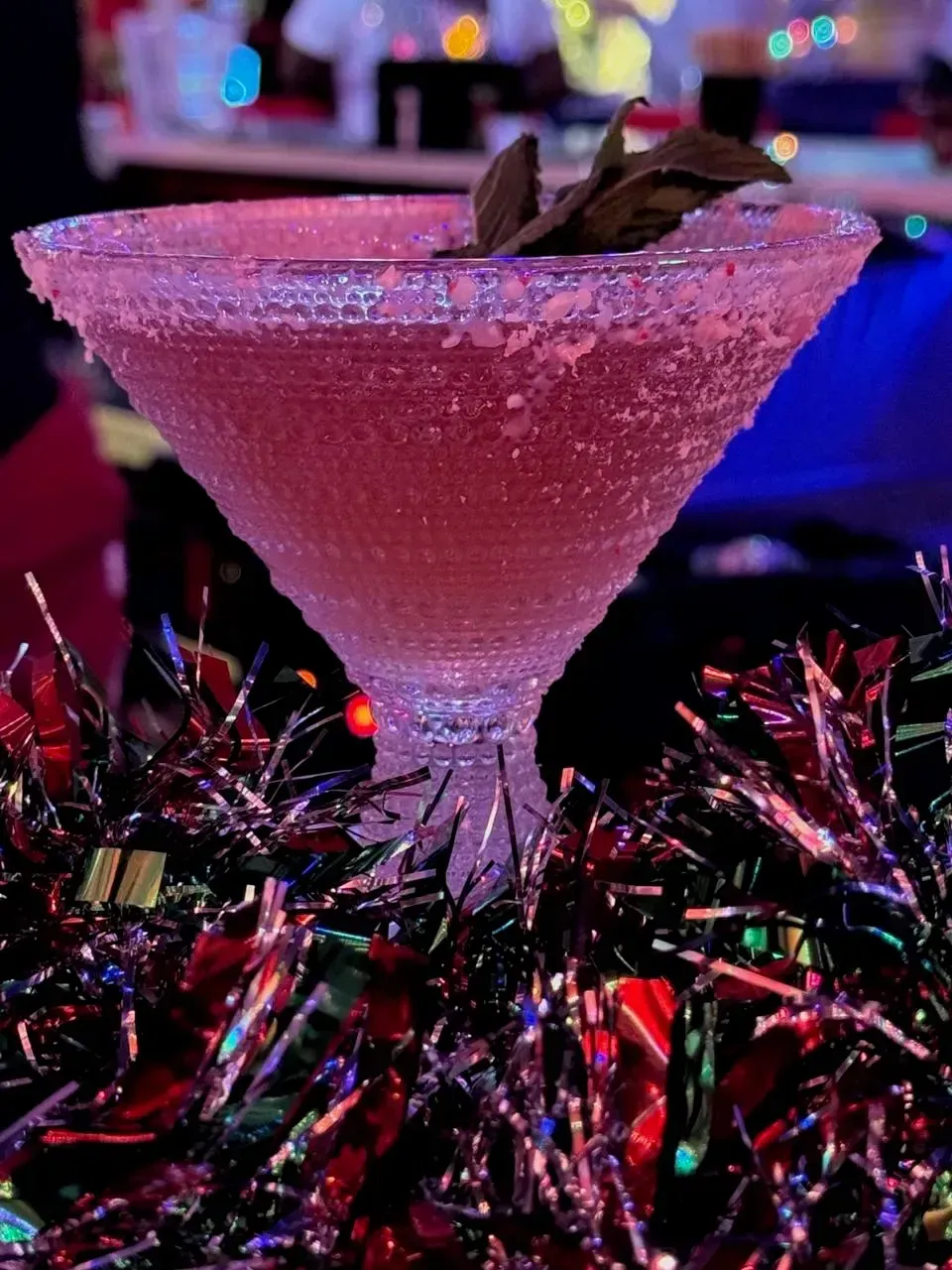 Pink cocktail in a sugared glass rim, garnished with mint, on tinsel.