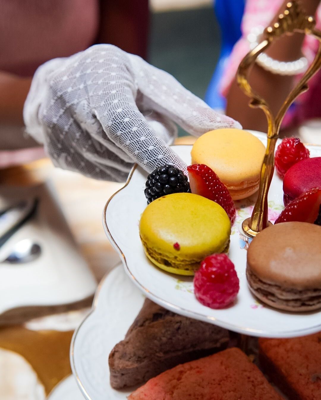 A gloved hand holds a tiered serving tray with macarons and berries; party setting.