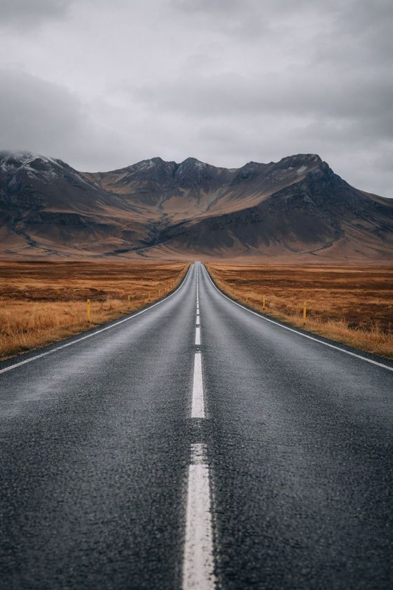 Een weg die zich uitstrekt richting de bergen onder een bewolkte hemel; een kaal landschap.