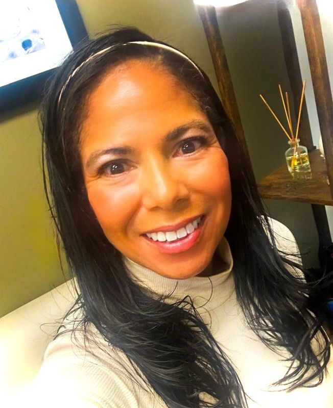 Woman wearing white shirt, smiles with an office background.