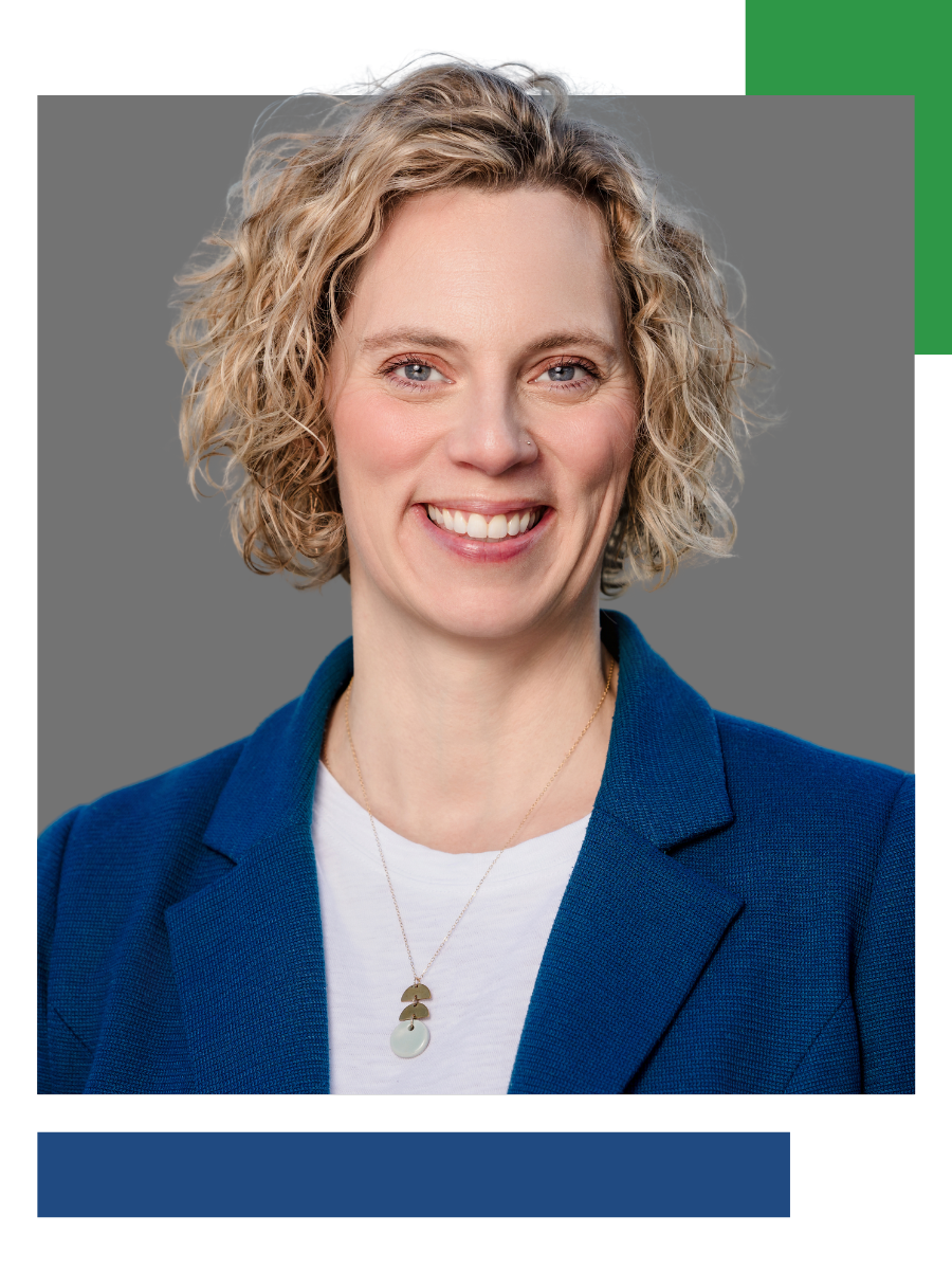 Woman with curly blonde hair, smiling, wearing a blue blazer and necklace, against a gray background.