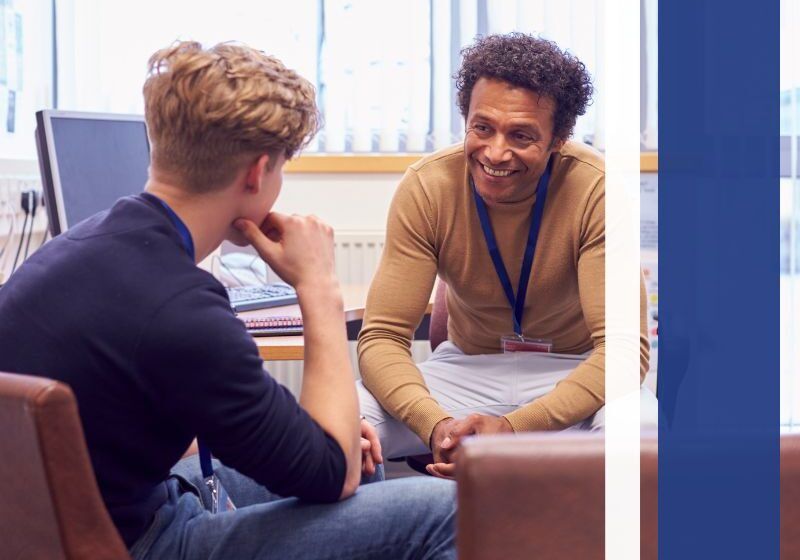A man smiles while speaking to another person in a seated discussion.