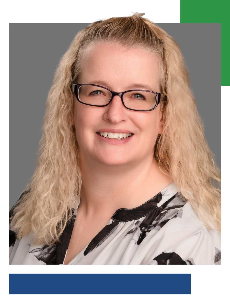Woman with glasses smiles; blonde hair, patterned blouse, professional headshot.