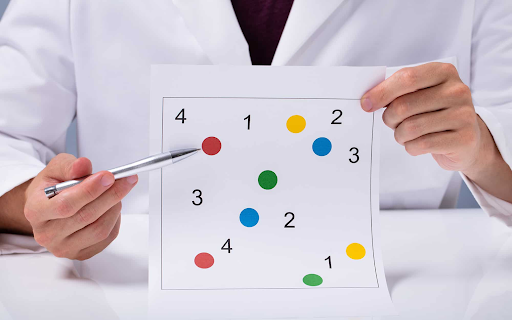 Doctor pointing at a sheet with colored dots and numbers, likely for a cognitive test.