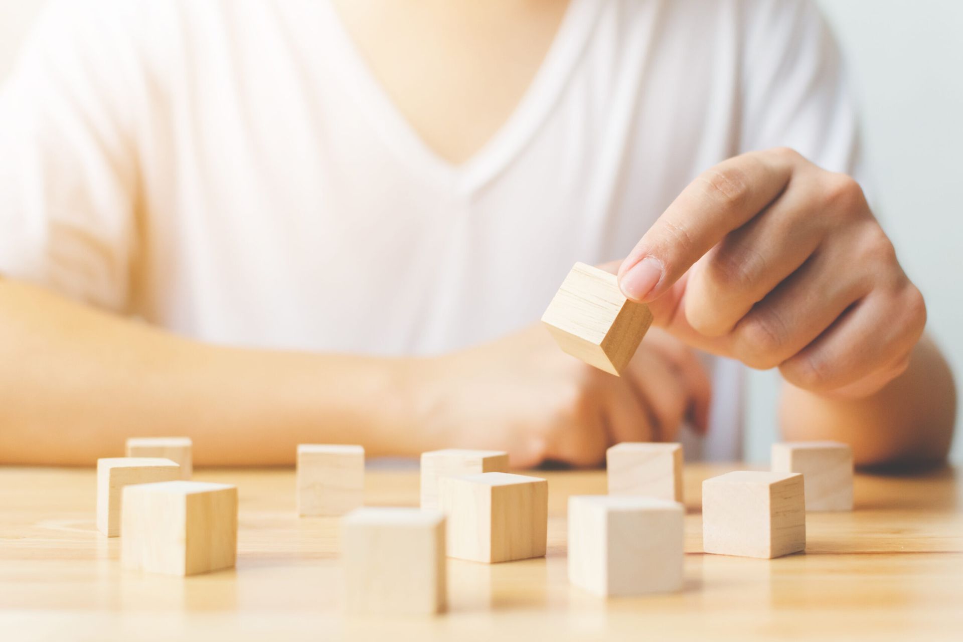 Person's hand placing a wooden block among other blocks on a wooden table.