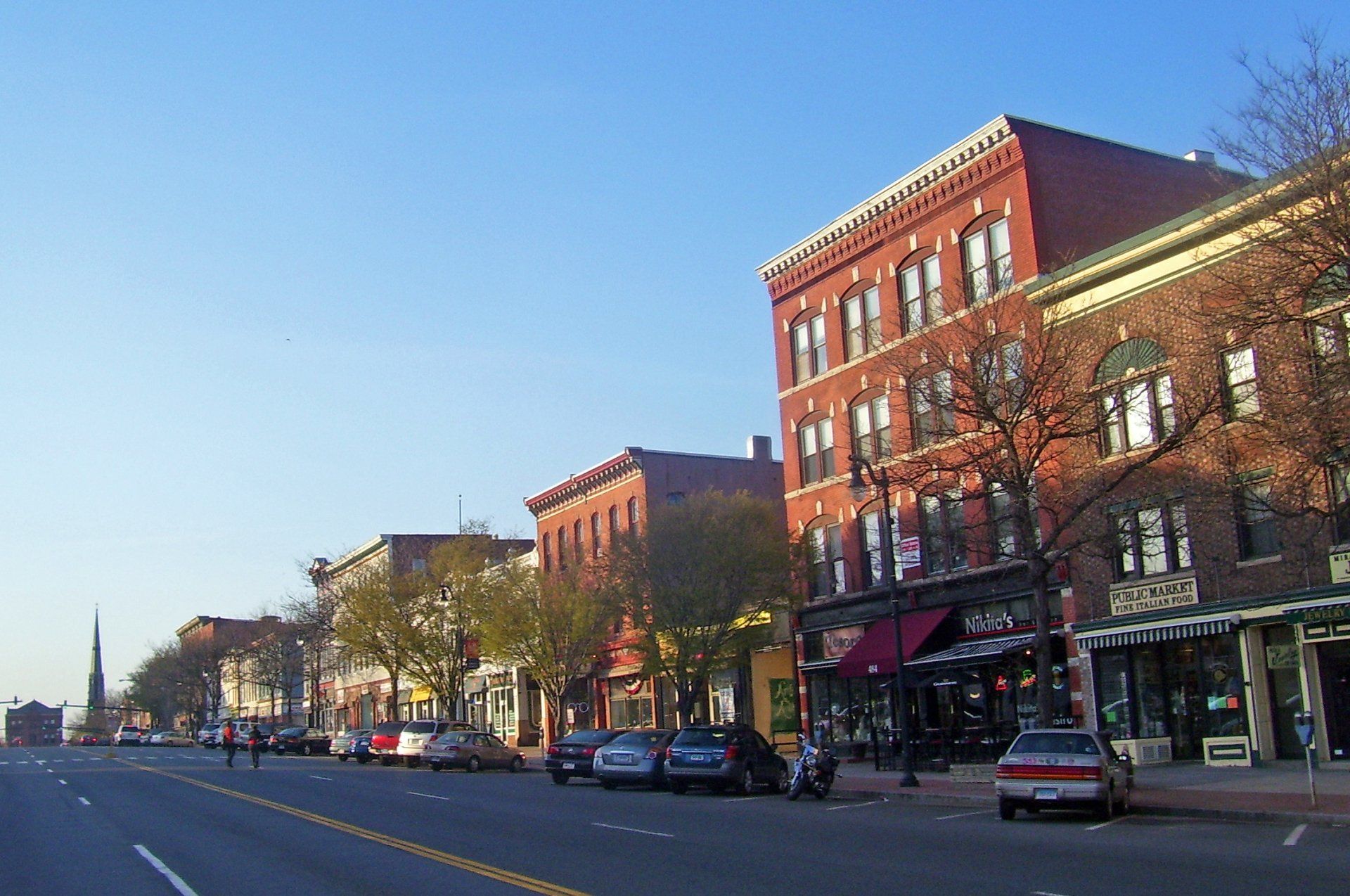 A row of brick buildings along a street with cars parked on the side of the road