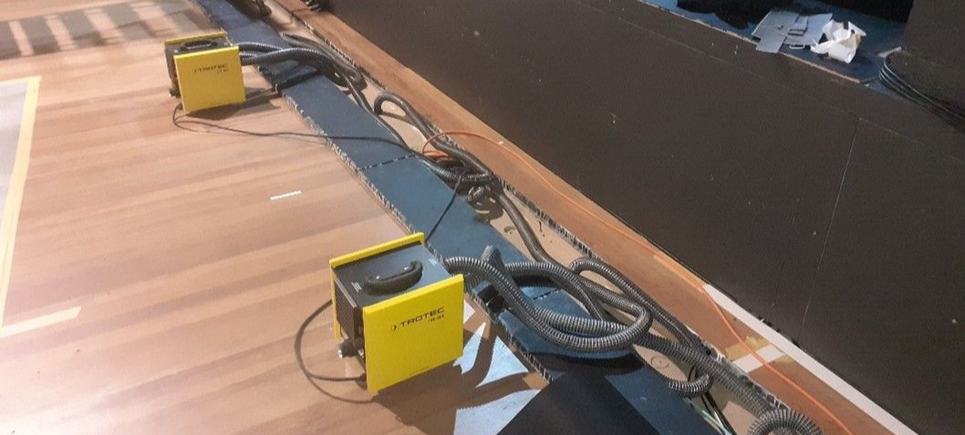 Zwei gelbe Kisten mit Kabeln auf einem Holzboden. Rechts befindet sich eine dunkle Wand.