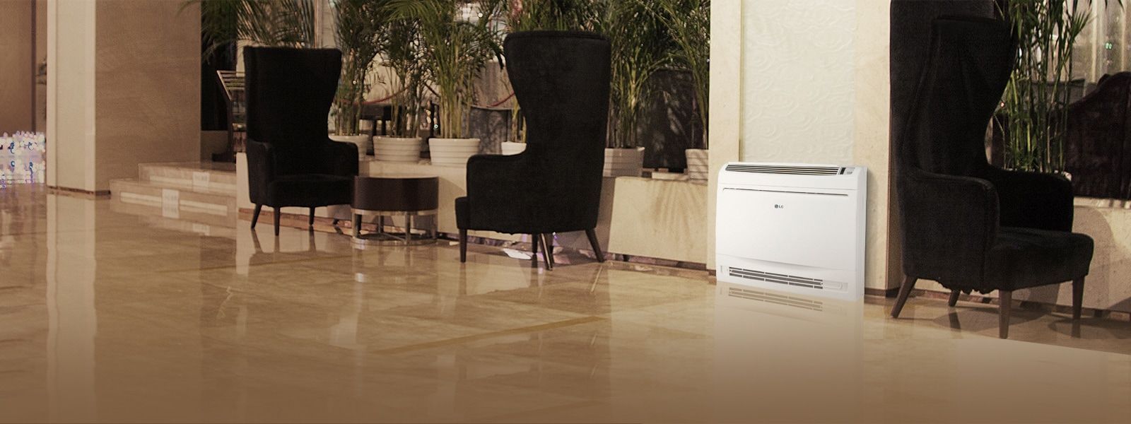 Die LG Console Luft-Luft-Wärmepumpe steht in einem Wohnzimmer in einer modernen Lobby mit schwarzen Ohrensesseln und grünen Pflanzen.