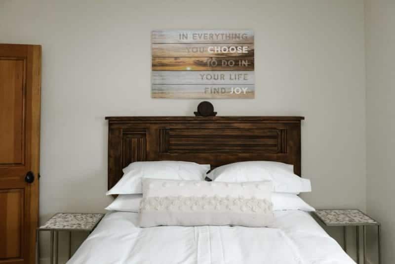 A bed with white sheets and pillows in a bedroom with a painting on the wall above it.