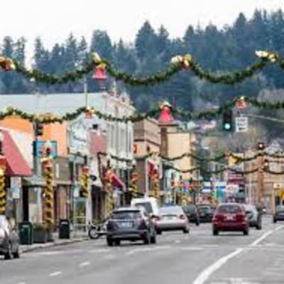 A busy street in a small town decorated for christmas with cars driving down it.