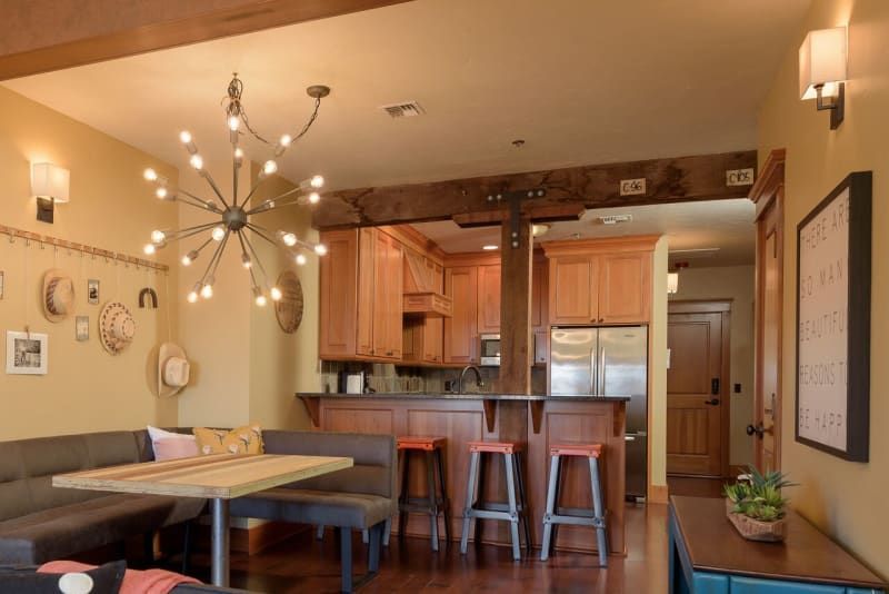 A living room with a table and stools and a kitchen in the background.