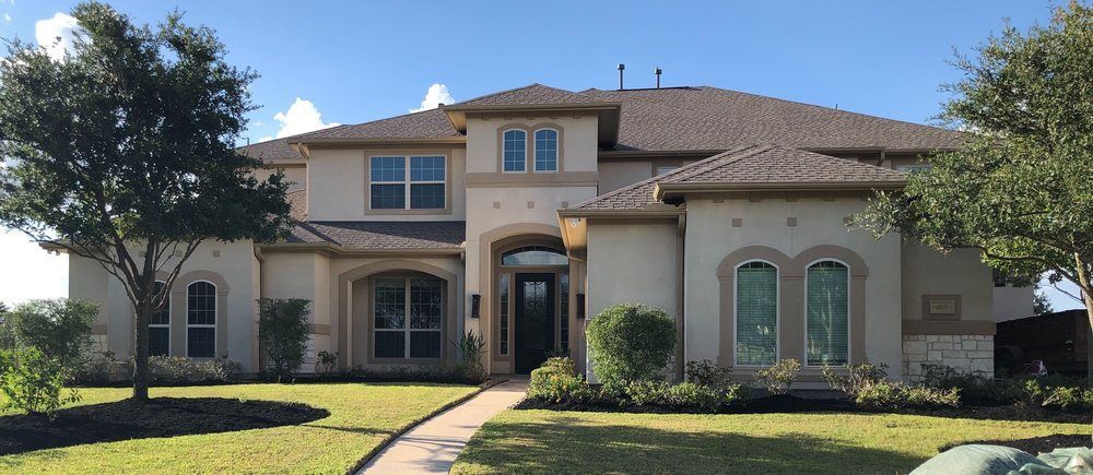 Exterior view of a beige two-story house with a tiled roof, lush green lawn, and a winding walkway to the front door.