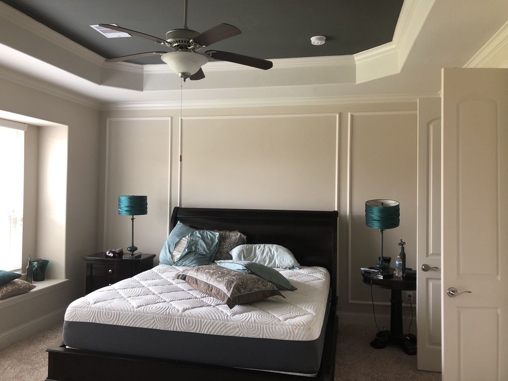 Bedroom with a dark bed, teal lamps, and a gray ceiling.