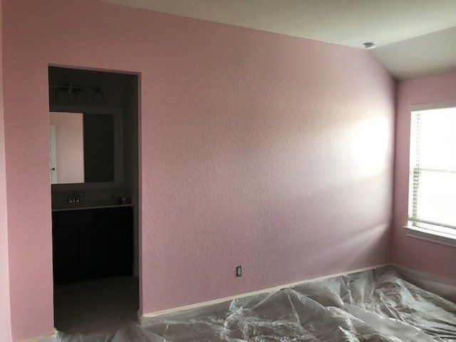 Pink-painted bedroom interior with doorway to a bathroom. The room has a window and protective plastic on the floor.