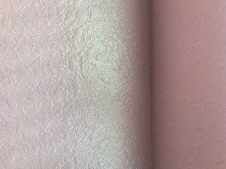 Pink walls meeting at a corner, one textured, one smooth.