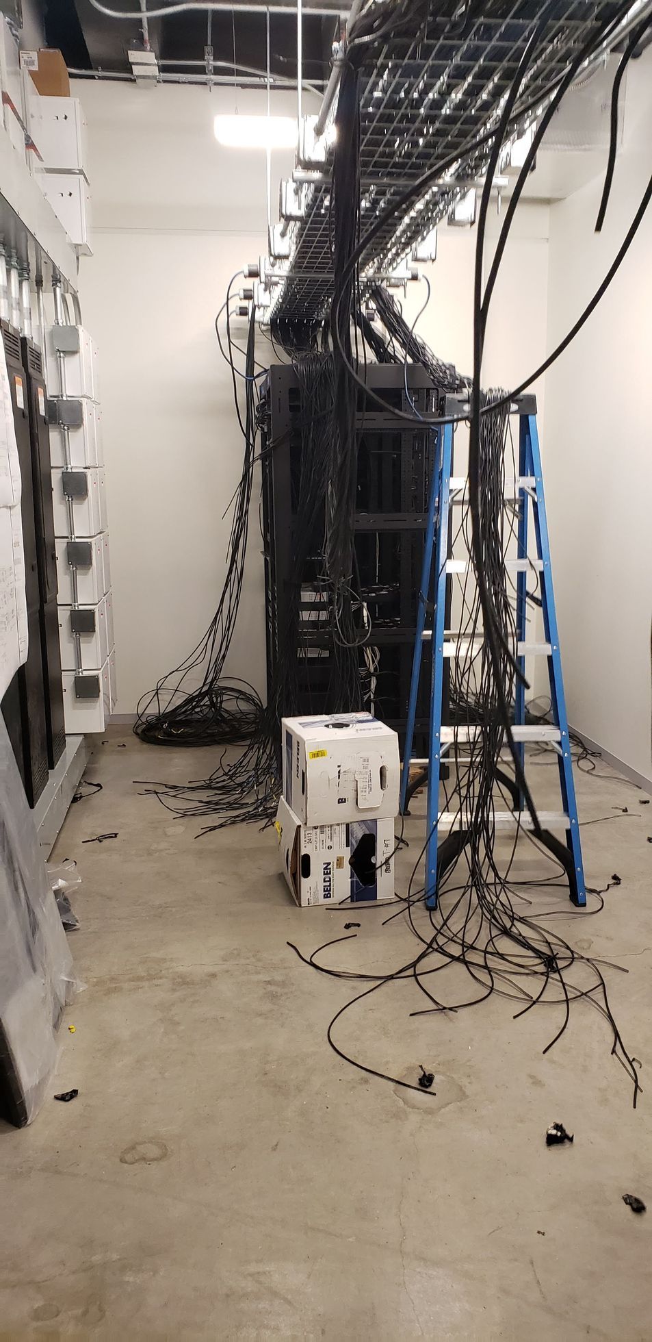 A room with a lot of wires hanging from the ceiling and a ladder.