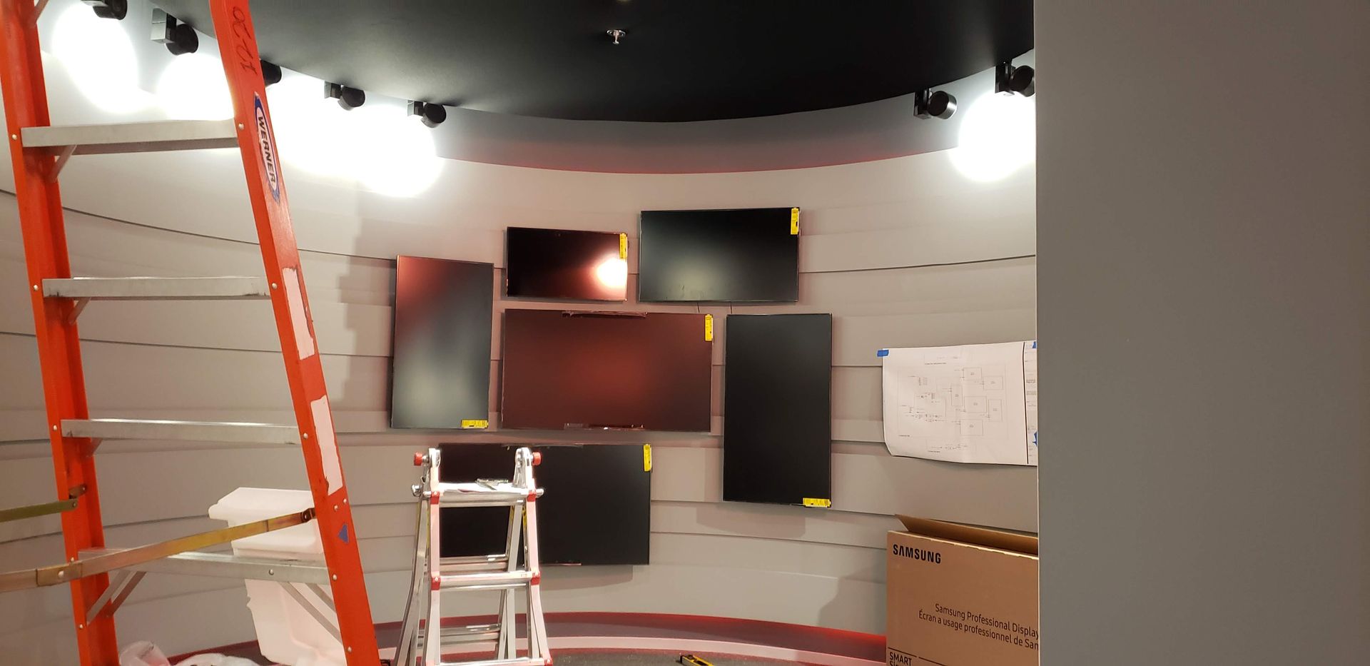 A room with a ladder and a bunch of monitors on the wall
