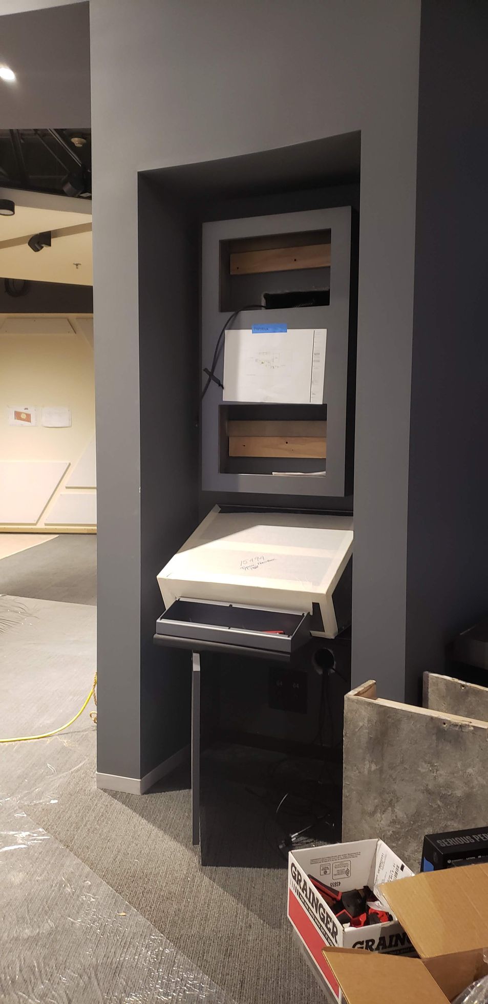 A printer is sitting in a corner of a room next to a box.