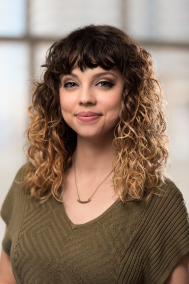 A woman with curly hair is wearing a green sweater and a necklace.
