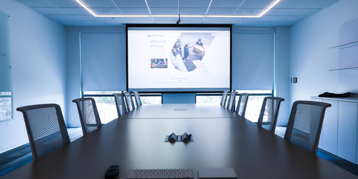 A conference room with a long table and chairs and a projector screen.