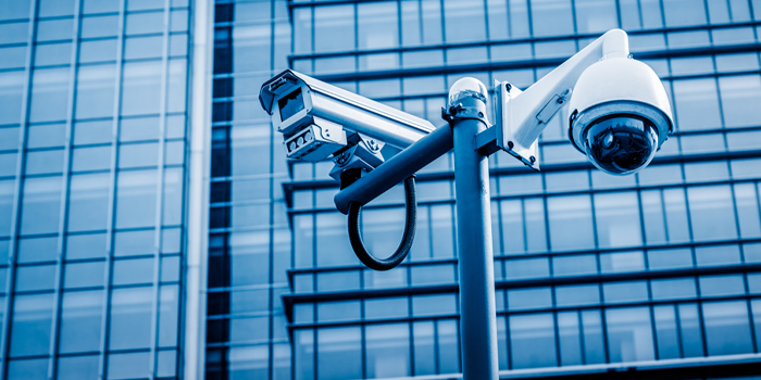 Two security cameras are sitting on a pole in front of a building.