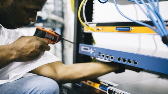 A man is working on a server with a screwdriver.