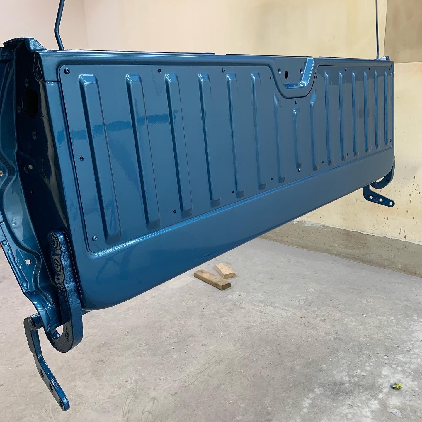 Blue pickup truck bed side panel leaning against a wall in a workshop or garage.