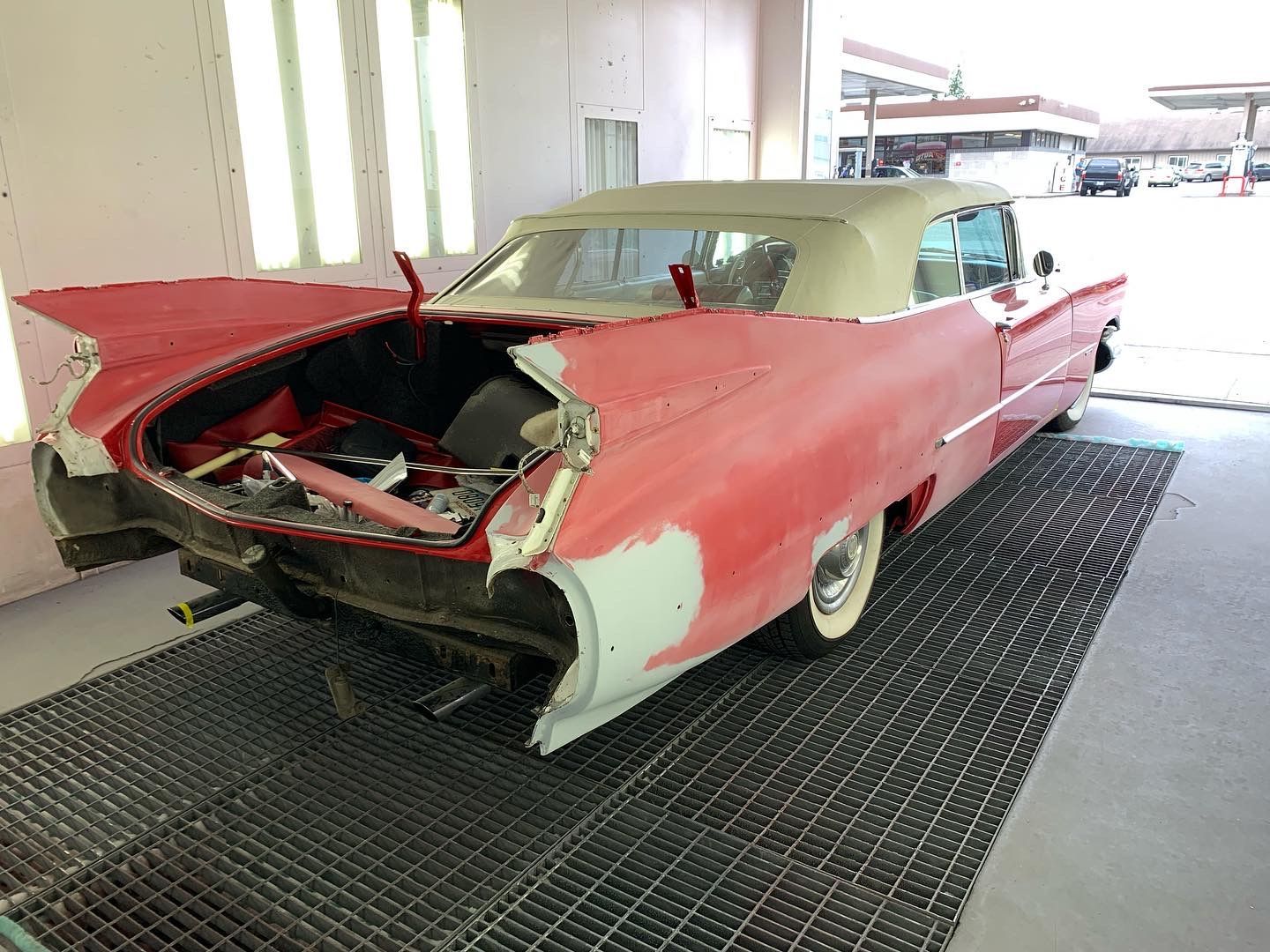 Damaged red classic car with front end removed, parked indoors on a black mat.