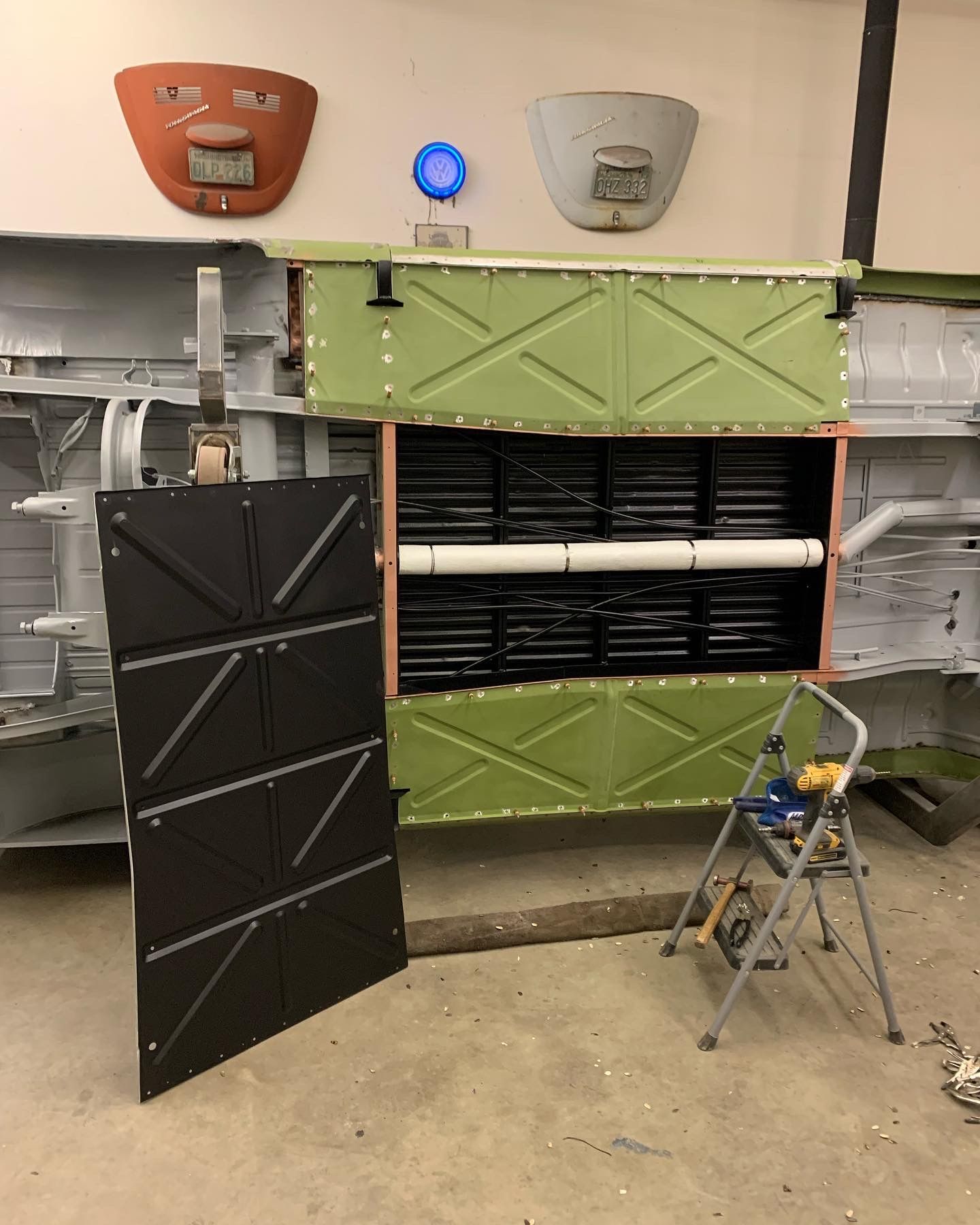 Open industrial wall cabinet with green and black panels, showing internal equipment and a step stool nearby.