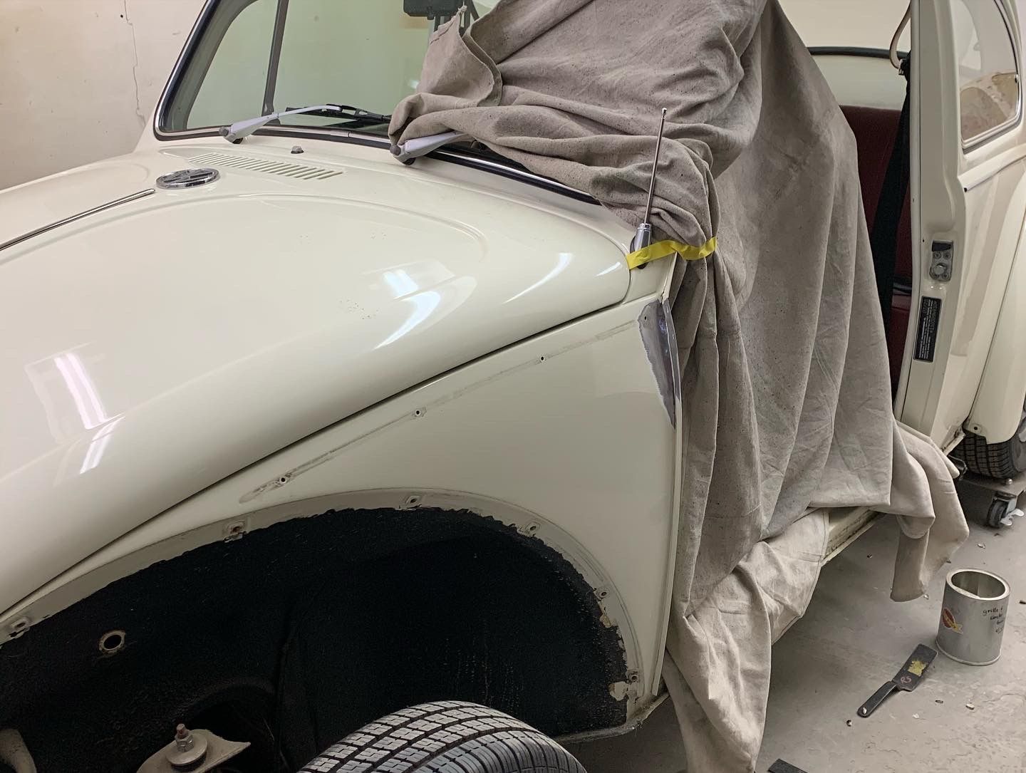 Person working on a white car body in a garage, covered with gray protective cloths and tools nearby