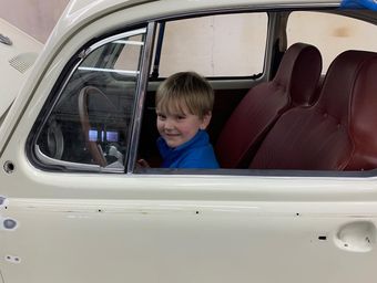 Smiling child sitting inside a cream-colored vintage car with red seats